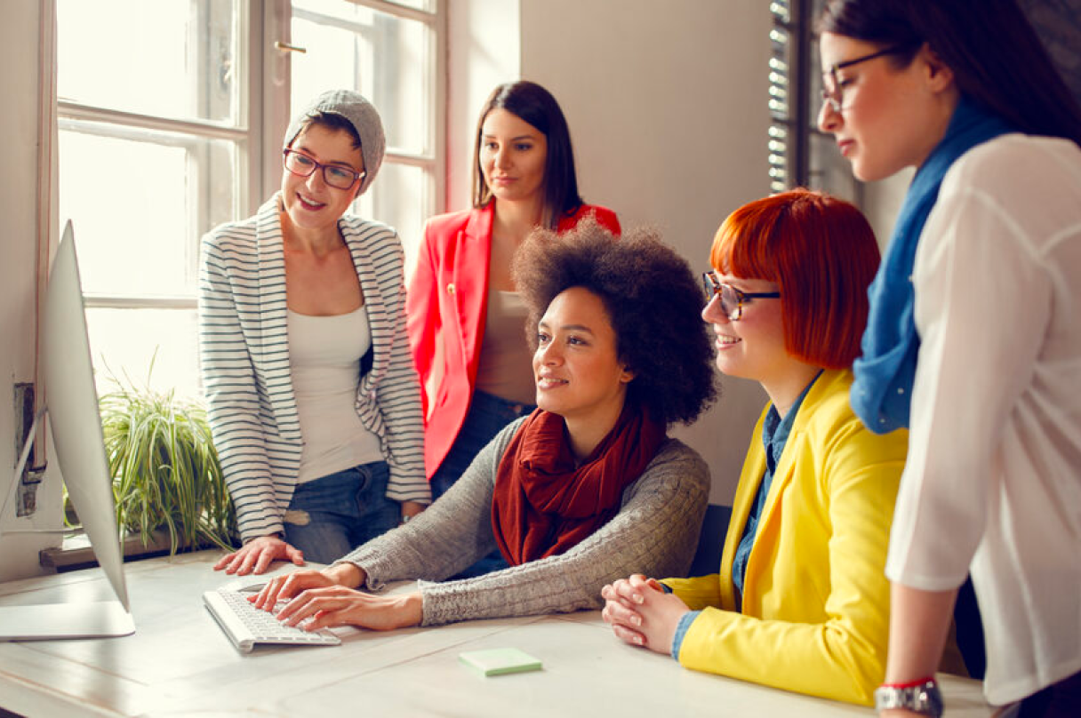 A group of woman gathered around a computer focusing on the computer screen.
